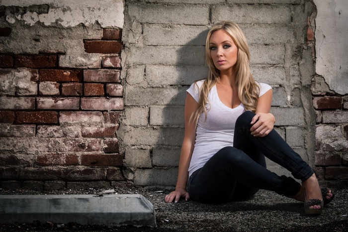 Blonde woman sitting by a brick wall