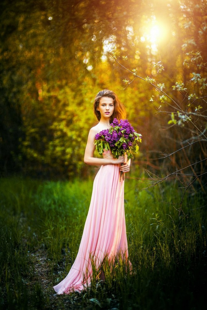 Woman in pink dress holding lilac flowers outdoors