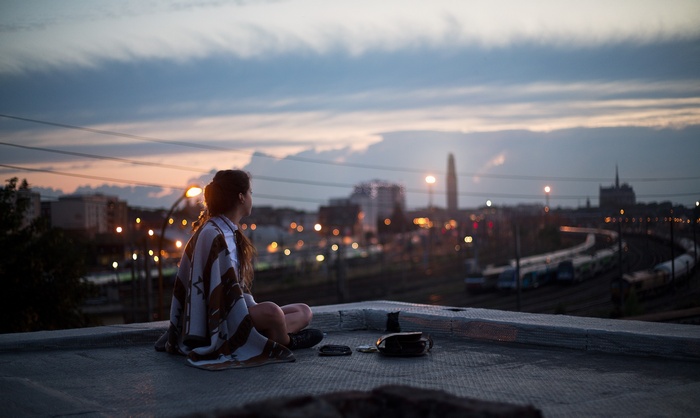 Woman sitting on a rooftop overlooking a city at dusk