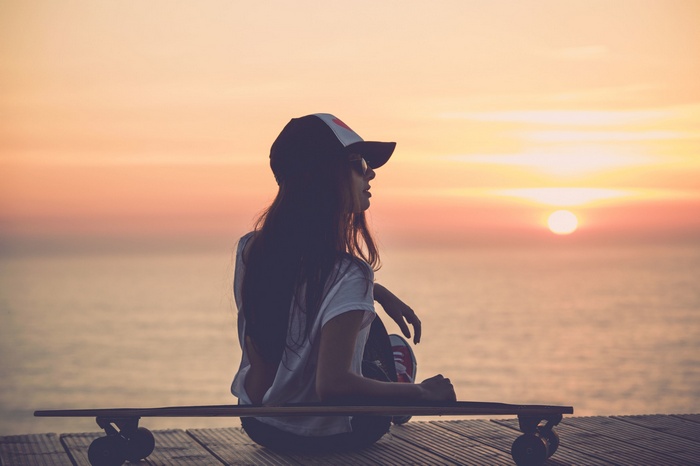 Woman with skateboard watching the sunset over the sea