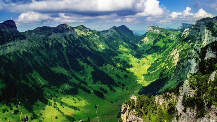 Green valley between mountains with trees and clouds