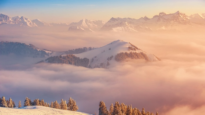 Snowy mountains above clouds at sunrise