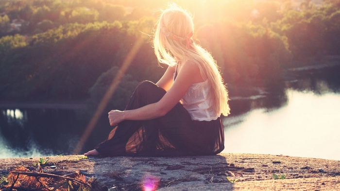 Woman sitting on a cliff overlooking a lake at sunset
