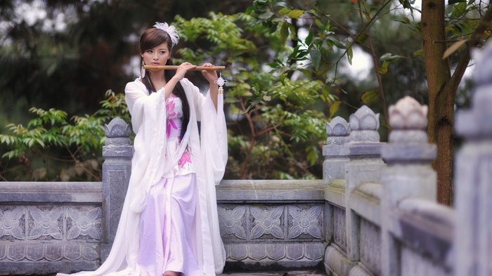 Woman in white dress playing a flute outdoors