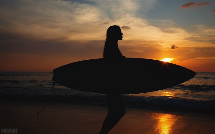 Viki Odintcova with a surfboard at sunset