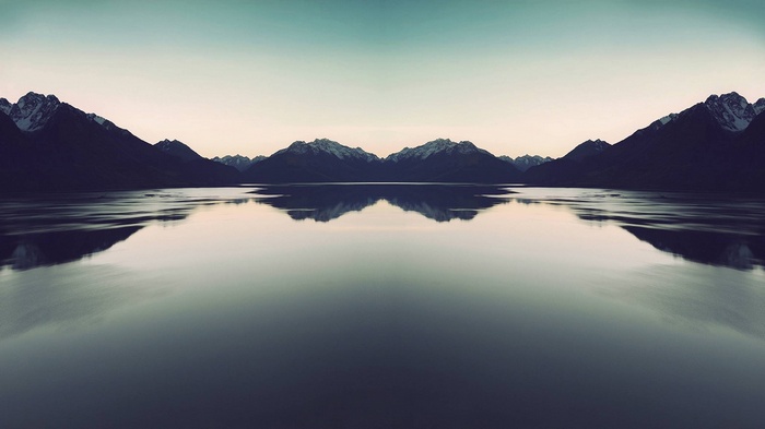 Symmetrical mountain range reflected in a calm lake at dusk