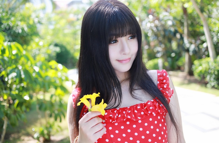 Asian woman in red polka dot dress holding yellow flower