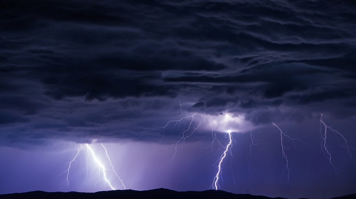 Lightning strikes over dark hills during a storm