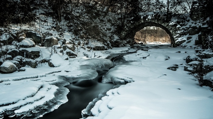 Stone bridge over a frozen stream in winter