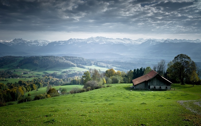 Barn on a grassy hill with mountains in the background
