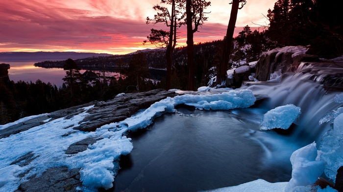 Winter sunset over a frozen lake with a waterfall