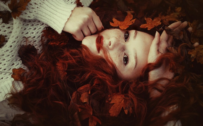 Redhead woman with freckles lying among autumn leaves