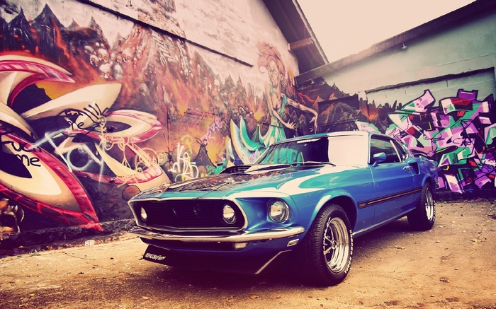 Blue Ford Mustang Mach 1 parked in front of graffiti wall
