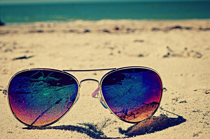 Aviator sunglasses on a sandy beach with the ocean in the background