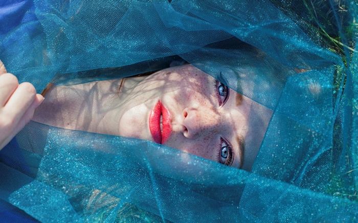 Woman with blue eyes and freckles under blue fabric