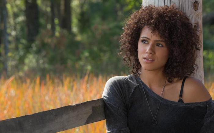 Nathalie Emmanuel leaning on a wooden post
