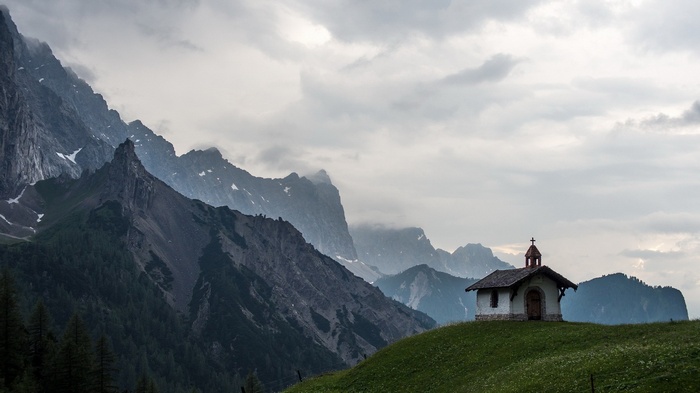 Small church on a grassy hill with mountains