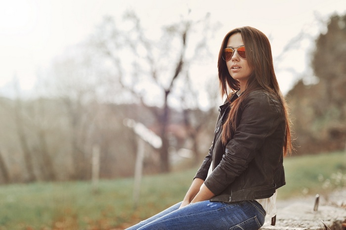 Woman with sunglasses and jeans sitting outdoors