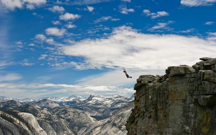 Man jumps off a cliff in a mountainous landscape