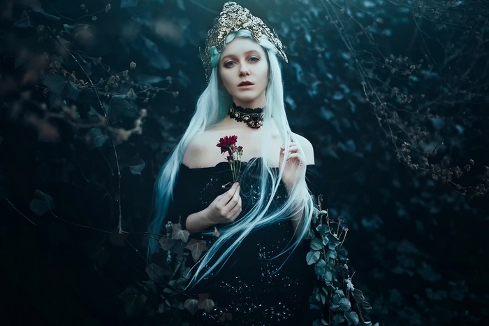 Woman with pale blue hair and crown holding a flower