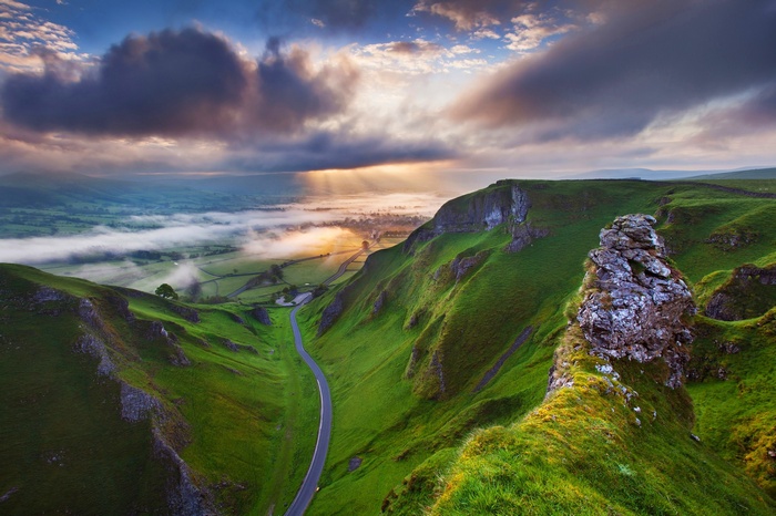Sun rays over a valley with a road and hills