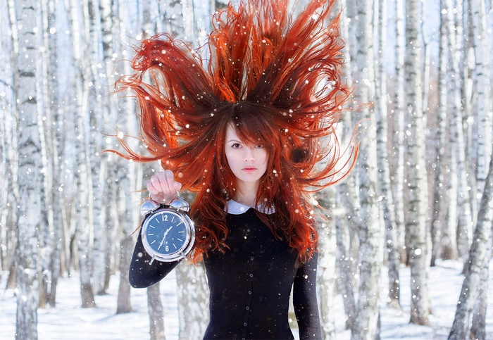 Redhead woman holding alarm clock in snowy birch forest