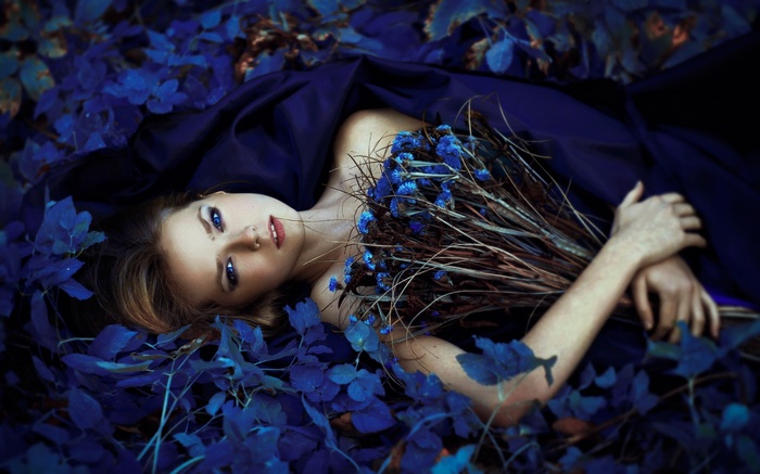 Woman with blue eyes lying in blue leaves with bouquet