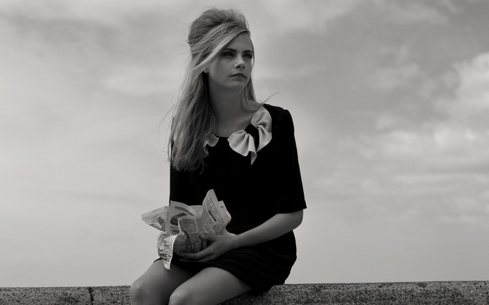 Cara Delevingne sitting outdoors holding crumpled paper