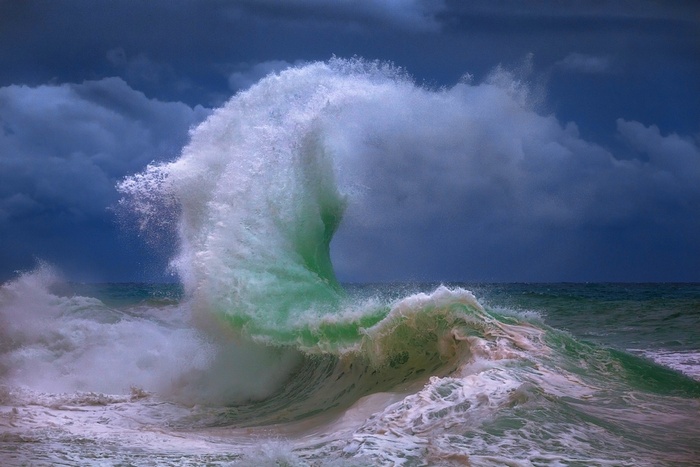 A powerful wave crashes under a stormy sky