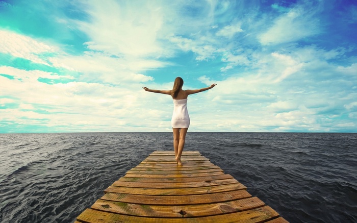 Woman in white dress on pier with arms outstretched