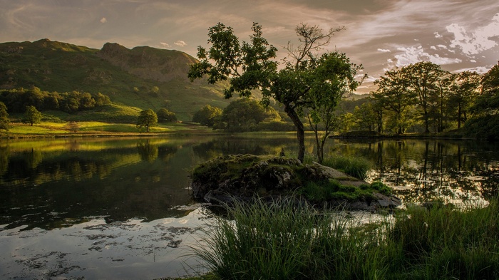 A tranquil lake reflects rolling hills and trees at sunset