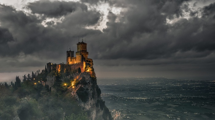 Castle on a cliff under dark clouds overlooking a cityscape