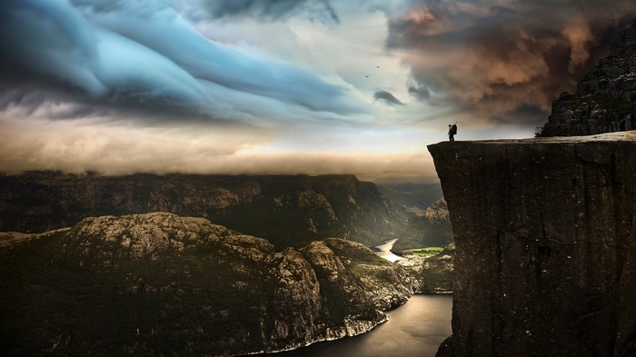 Man standing on cliff overlooking a fjord in Norway