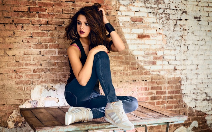 Selena Gomez sitting on a wooden table in front of a brick wall