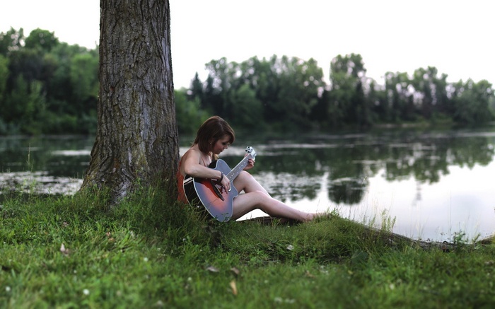 Woman playing guitar by a lake in a forest