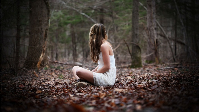 Woman in white dress sitting in a forest with fallen leaves