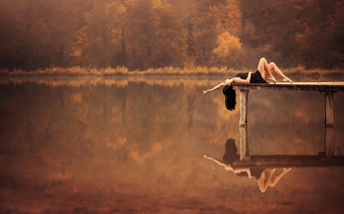 Woman in black dress lying on a pier over a lake
