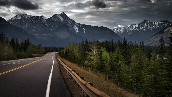 Road through mountains and forest under stormy clouds