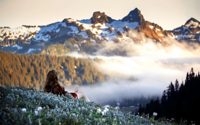 Woman sitting in a field overlooking misty mountains