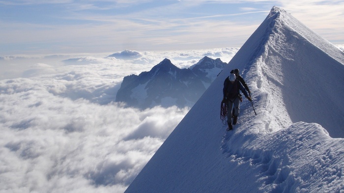 Two climbers on a snowy mountain ridge above clouds