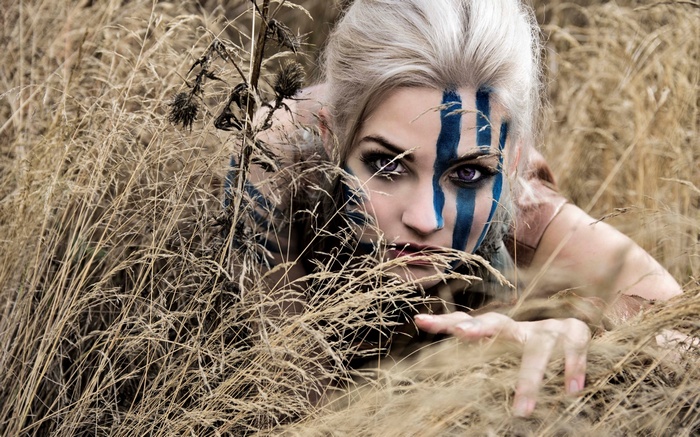 Woman with blue face paint in dry grass