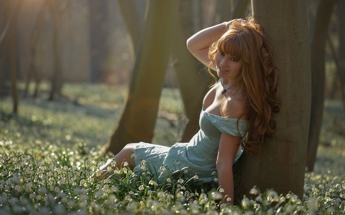Redhead woman in a dress sitting in a forest with flowers