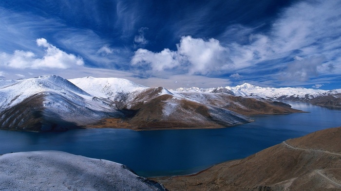 Snow-capped mountains surround a deep blue lake under a cloudy sky
