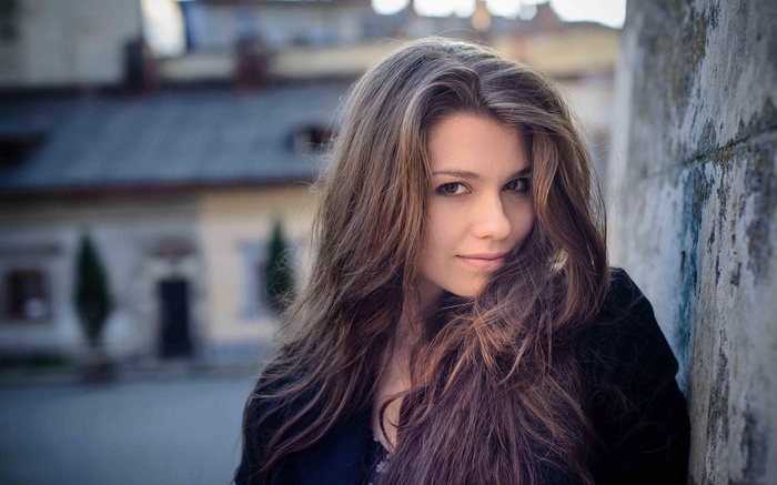 Woman with long brown hair leaning against a wall