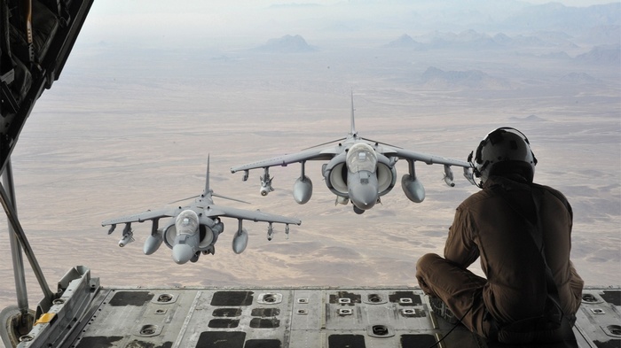 Two AV-8B Harriers fly over a desert landscape