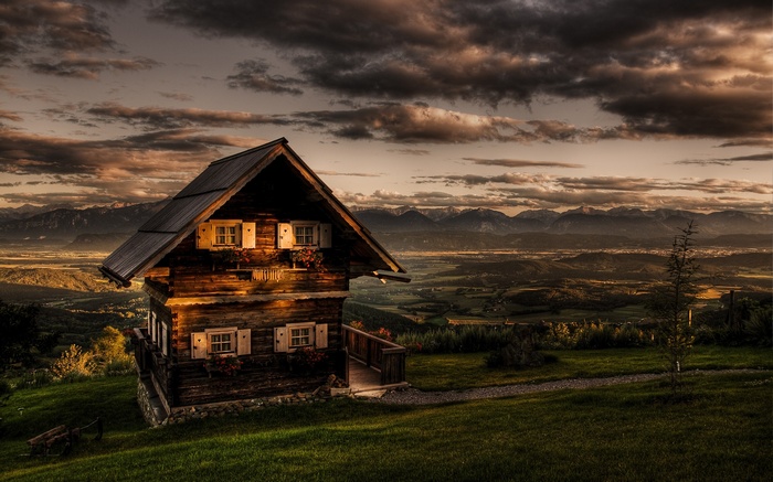 Wooden house on a hill overlooking mountains at sunset