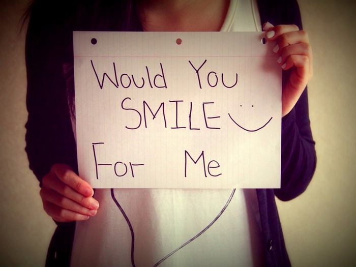 Woman holding a sign that says "Would You Smile For Me"