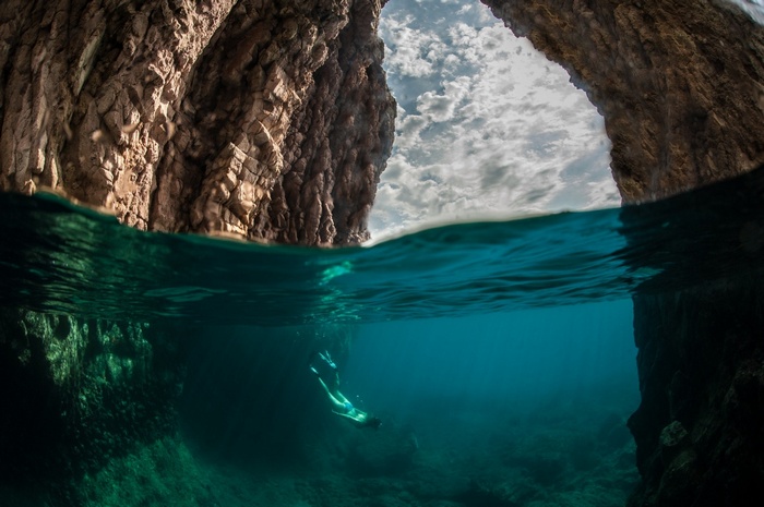Split view of a diver in a sea cave with rocky cliffs
