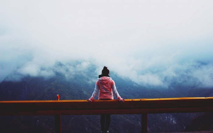 Woman sitting on a guardrail overlooking mountains