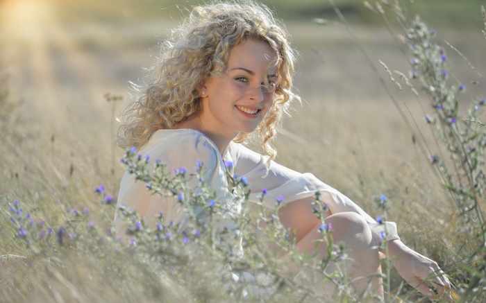 Woman with curly blonde hair sitting in a field